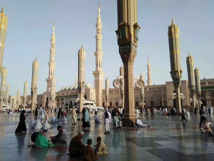 a group of people sitting on the ground in front of a building, a picture, hurufiyya, cybermosque interior, golden pillars, black domes and spires, very long spires