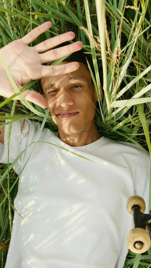 a man laying in the grass with a skateboard, by Andries Stock, land art, portrait of chester bennington, low quality photo, selfie photo, in the high grass