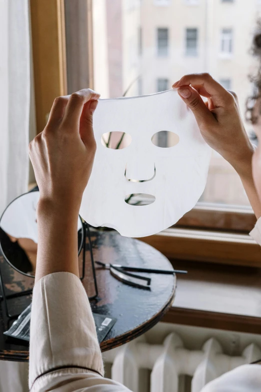 a woman holding a piece of paper in front of a window, some of them use gask mask, perfectly lit face, silicone skin, botanicals