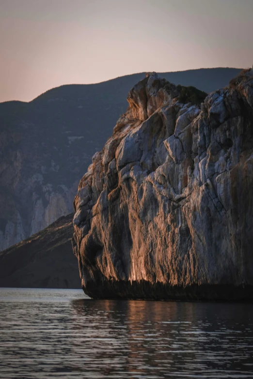 a large rock in the middle of a body of water, at the golden hour, steep cliffs, byzantine, islands