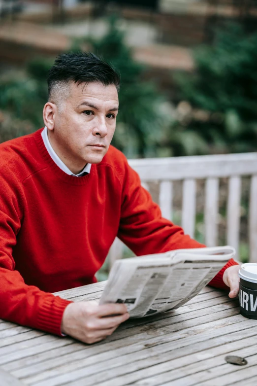 a man sitting at a table reading a newspaper, inspired by Eddie Mendoza, wearing red, lgbtq, in london, temuera morrison