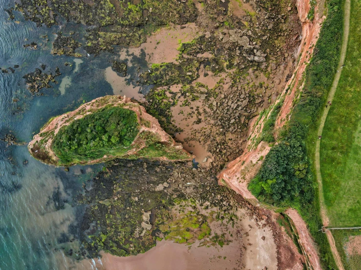 a large body of water next to a lush green hillside, an album cover, by Adam Marczyński, pexels contest winner, red sand beach, erosion channels river, top down perspecrive, maryport