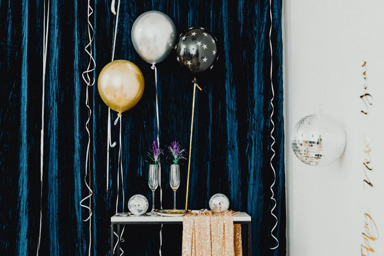 a table that has a bunch of balloons on it, a still life, by Julia Pishtar, trending on unsplash, glittering silver ornaments, curtains, college party, gold and indigo