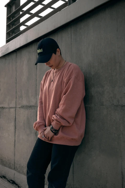 a man leaning against a wall with a skateboard, trending on unsplash, realism, wearing a pastel pink hoodie, baggy clothing and hat, wearing sweatshirt, male ulzzang