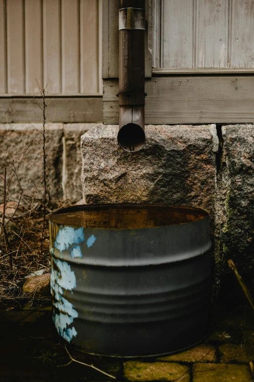 a metal barrel sitting on the side of a building, by Jesper Knudsen, unsplash, stream flowing through the house, drainpipes, brown, low quality photo