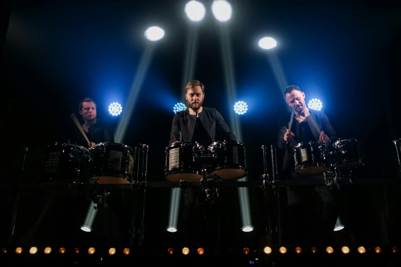 a group of men standing on top of a stage, bongos, liam, subtle and compelling lighting, with robotic arms