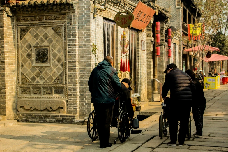 a group of people walking down a street next to a building, inspired by Cui Bai, pexels contest winner, wheelchair, ancient china, old village, thumbnail