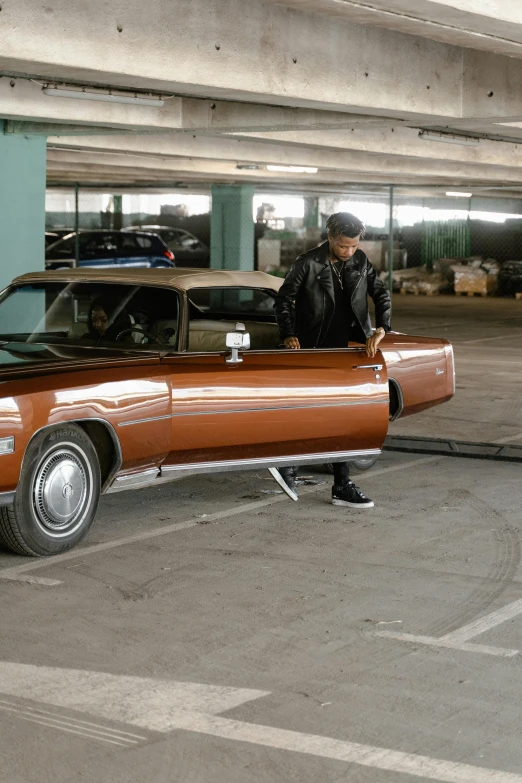 a man standing next to a car in a parking garage, an album cover, lowriders, b - roll, stretch, on ground