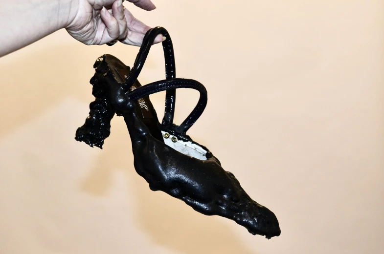 a close up of a person holding a pair of shoes, an album cover, by Ellen Gallagher, new sculpture, dripping black goo, heels, molten plastic, black jewellery