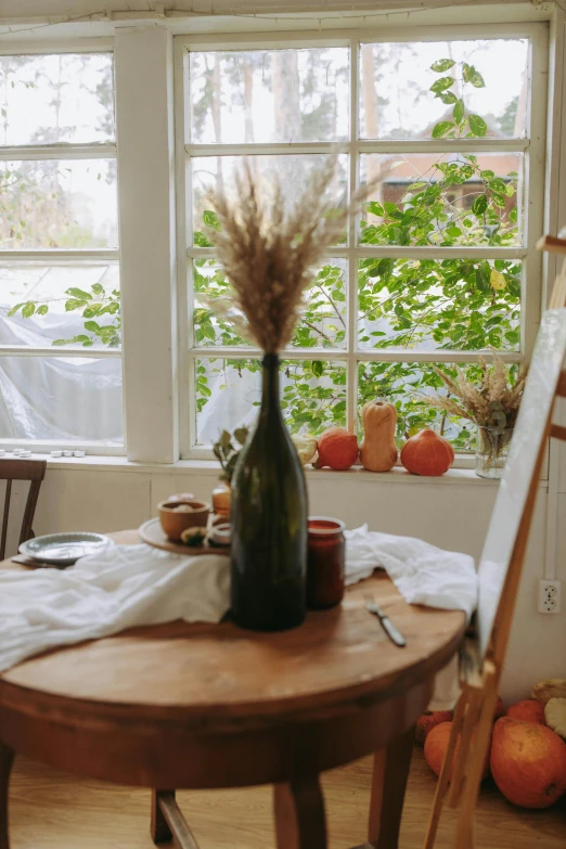 a painting easel sitting on top of a wooden table, a still life, by Jessie Algie, pexels contest winner, bay window, autum, chefs table, hay