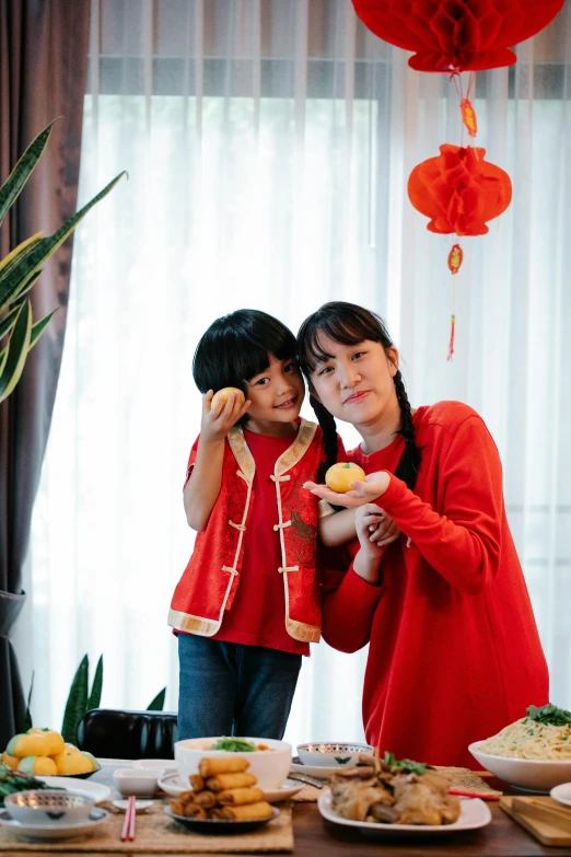 a couple of women standing next to each other at a table, inspired by Cui Bai, symbolism, wearing a red outfit, with a kid, holding a tangerine, #trending