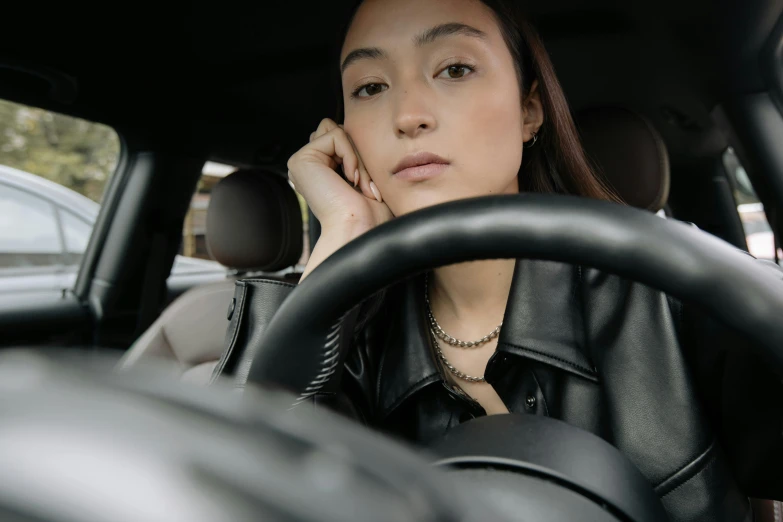 a woman sitting behind the wheel of a car talking on a cell phone, trending on pexels, photorealism, portrait sophie mudd, sleepy fashion model face, wearing black, slightly round chin