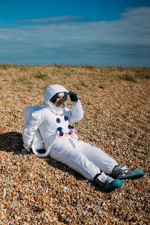 a man in an astronaut suit sitting on the ground, inspired by Alan Bean, unsplash, surrealism, seaside, dressed as a scavenger, slightly sunny, prince