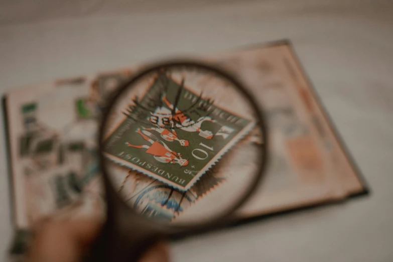 a person holding a magnifying glass over a stamp, by Emma Andijewska, pexels contest winner, cartography, hunting, postage, shot from below