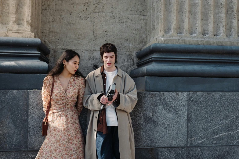 a couple of people standing next to each other, pexels contest winner, renaissance, light brown coat, looking at his phone, wearing a long flowery dress, movie footage