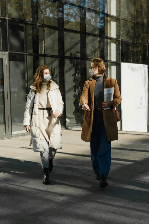 a couple of people walking down a street, trending on pexels, wearing a long coat, masked doctors, woman holding another woman, wearing cargo pants