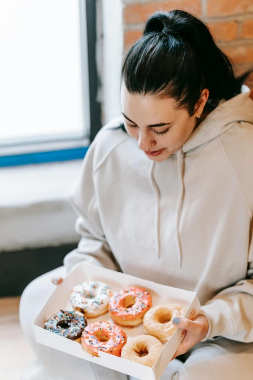 a woman sitting on the floor holding a box of donuts, pexels contest winner, wearing a hoodie and sweatpants, profile image, pastries, gal gadot china plate