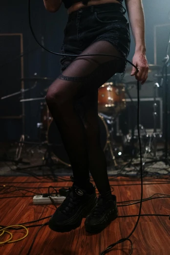 a woman standing on top of a wooden floor holding a microphone, inspired by Nan Goldin, antipodeans, tights, playing drums, pitch black room, thighs close up
