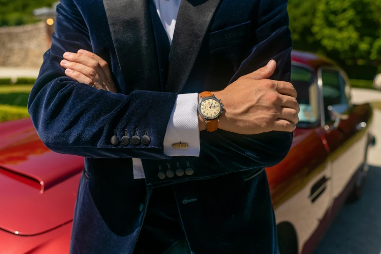 a man in a suit standing in front of a red car, inspired by Harry Haenigsen, trending on pexels, renaissance, gold watch, vintage aston martin, tan suit, top angle view