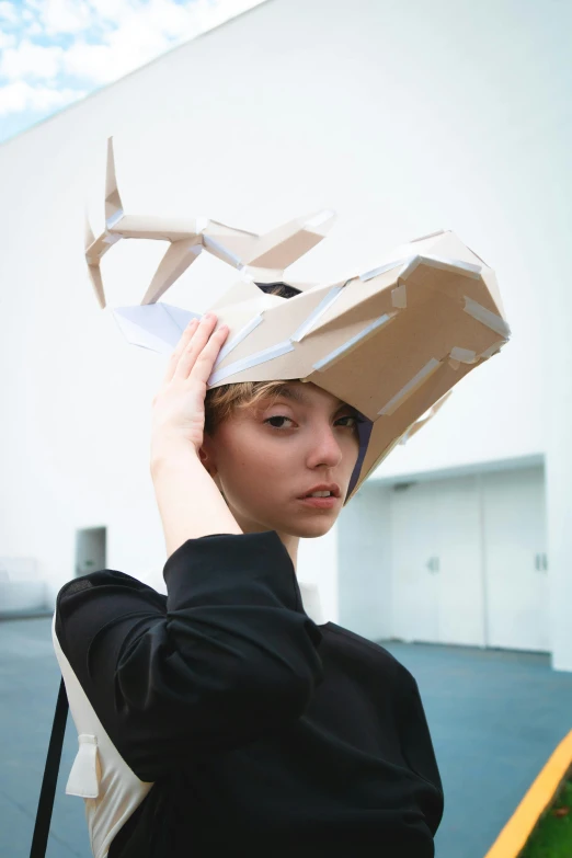 a woman with a cardboard box on her head, inspired by Tadashi Nakayama, tumblr, conceptual art, dragon shaped helmet, at a fashion shoot, gen z, origami