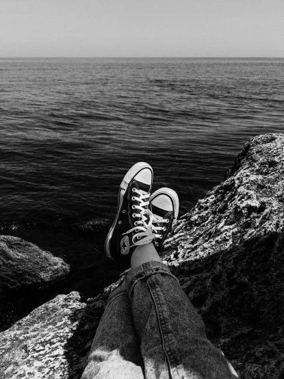 a person sitting on top of a rock next to the ocean, a black and white photo, by Alexis Grimou, sneakers, grunge aesthetic!!! (, anna nikonova, myself