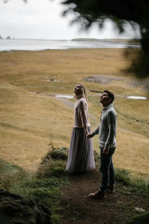 a man and woman standing on top of a hill, by Else Alfelt, unsplash contest winner, romanticism, looking to the side, high angle shot, grey, grass