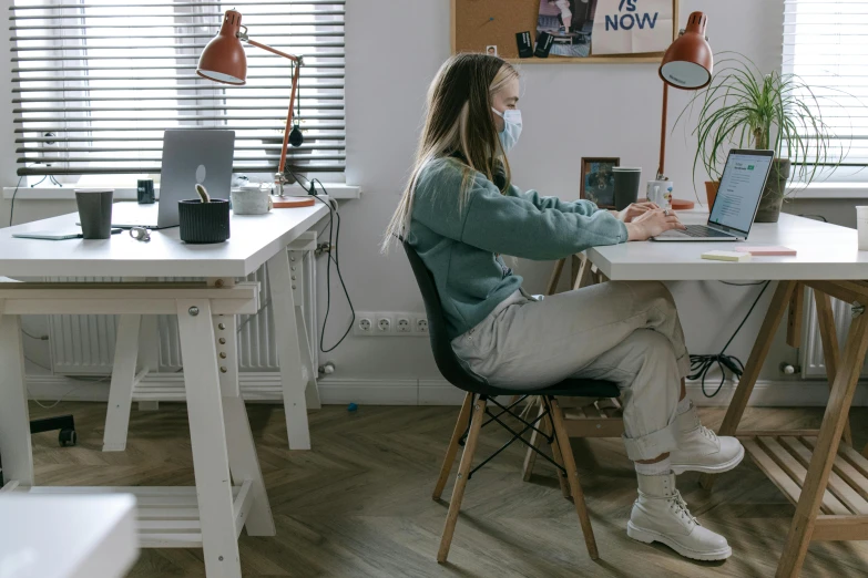 a woman sitting at a desk using a laptop computer, a colorized photo, trending on pexels, masked person in corner, sitting on designer chair, college students, open plan