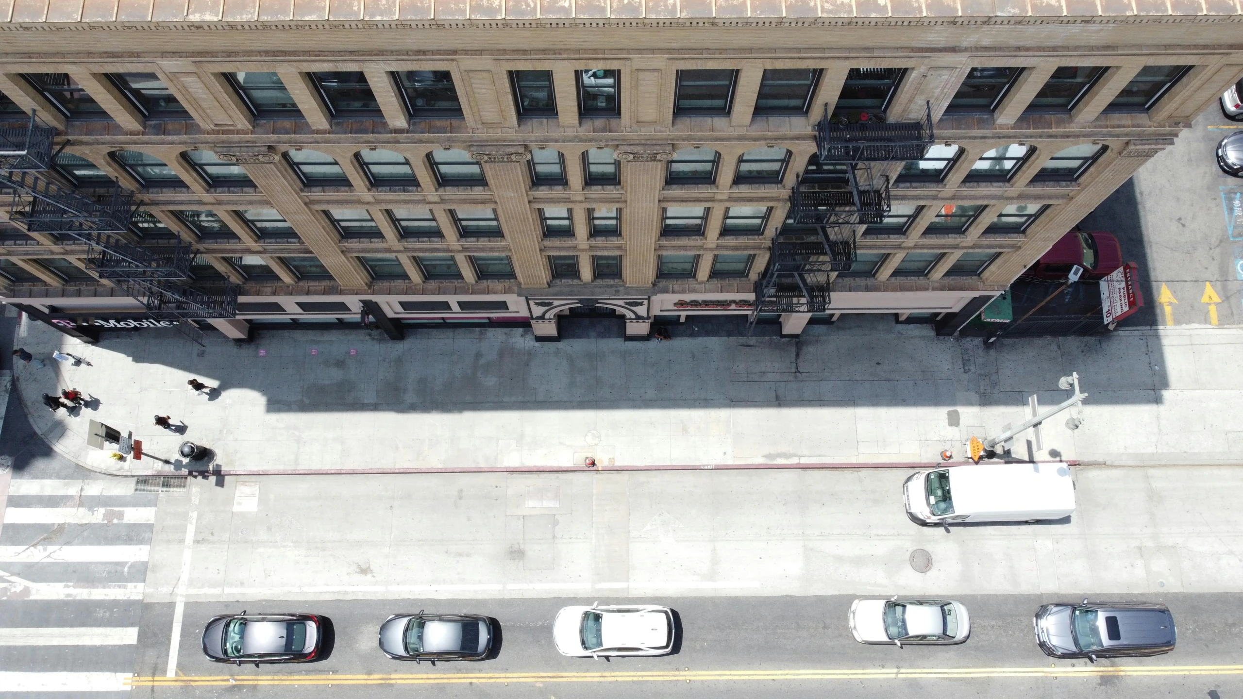 a group of cars driving down a street next to tall buildings, a photo, unsplash, photorealism, ignant, 2 d overhead view, hollywood standard, building facing