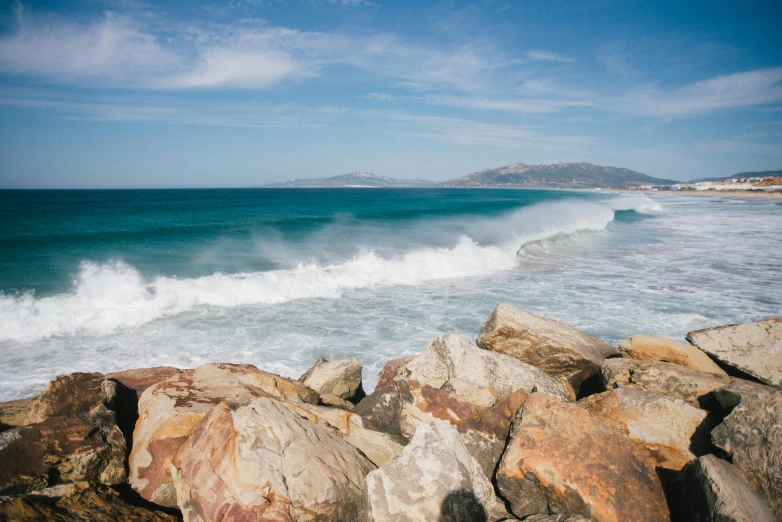 a person riding a surfboard on a wave in the ocean, pexels contest winner, waves crashing at rocks, hollister ranch, australian beach, rocky foreground