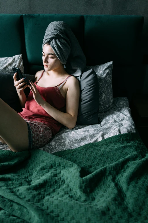 a woman sitting on a bed using a tablet computer, a photo, inspired by Elsa Bleda, trending on pexels, renaissance, queer woman, cell phone, long night cap, awkward