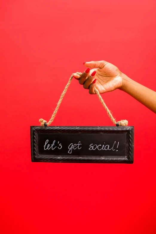 a woman holding a sign that says let's get social, by Rachel Reckitt, black on red, commercial product photography, made of smooth black goo, dark-skinned