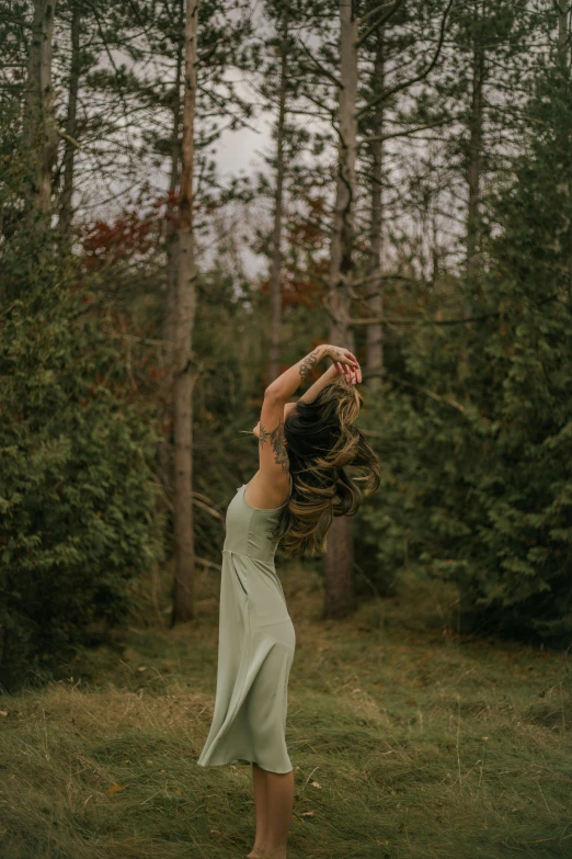a woman standing in the middle of a forest, arabesque, sassy pose, muted green, fall season, half turned around
