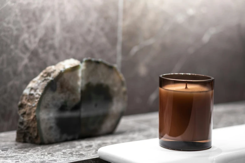 a candle sitting on top of a counter next to a rock, inspired by Nōami, unsplash, minimalism, brown resin, panels, extremely polished, brown