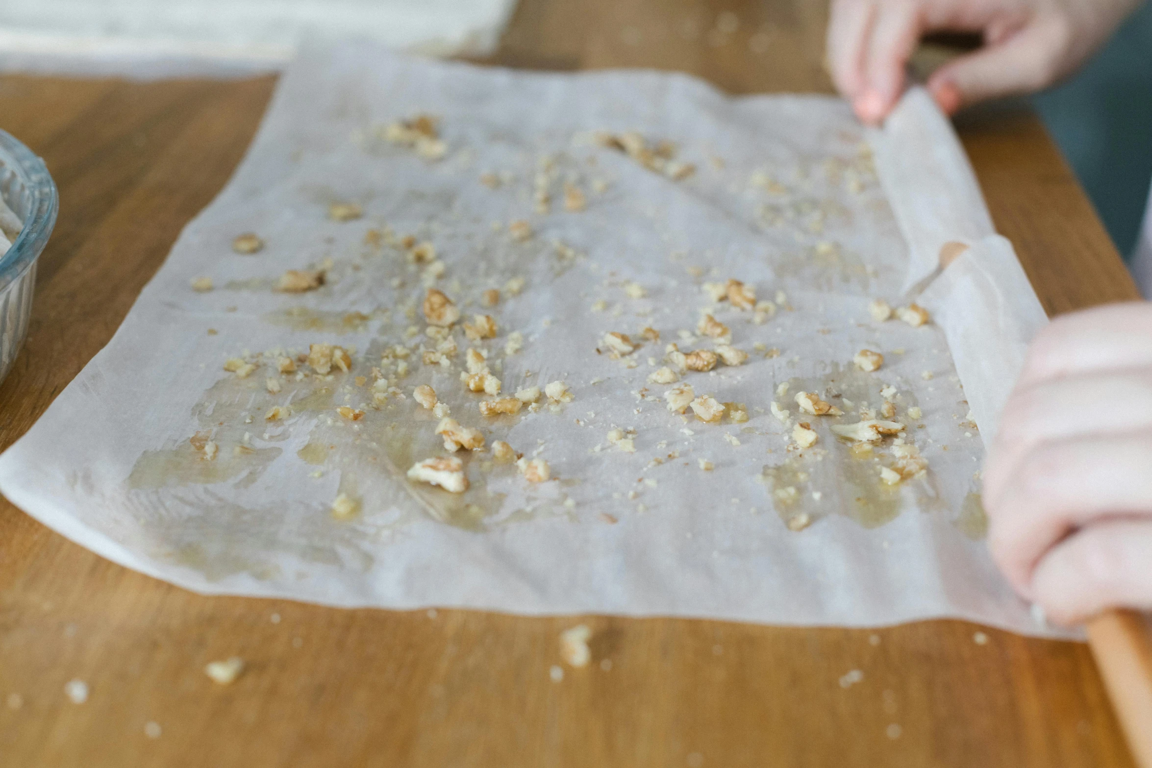 a close up of a person making food on a table, parchment paper, walnuts, scattered golden flakes, wet fabric