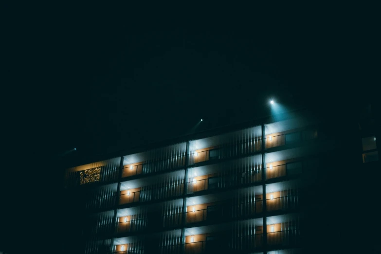 a tall building lit up at night with street lights, inspired by Elsa Bleda, unsplash contest winner, brutalism, hotel room, spooky photo, minimalist cinematic lighting, photo taken from the ground