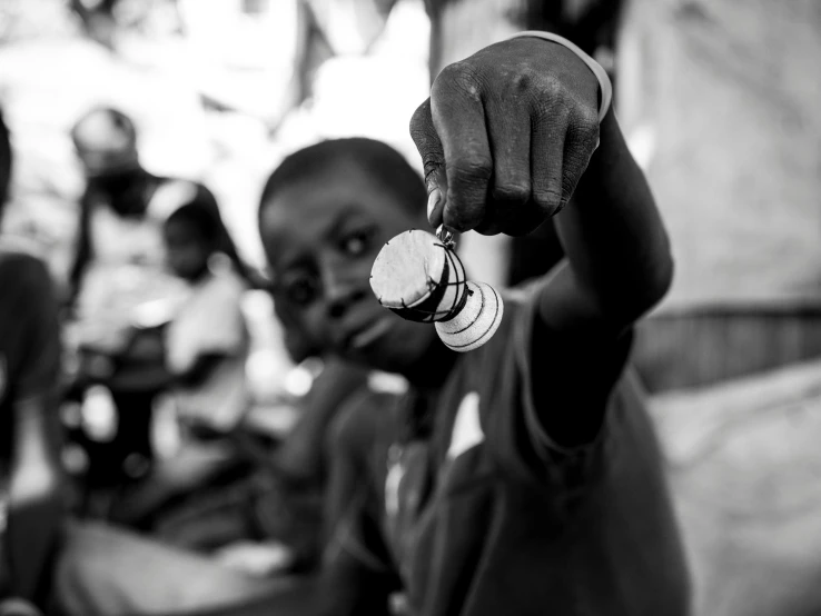 a black and white photo of a boy holding a coin, by Daniel Gelon, emmanuel shiru, offering the viewer a pill, school class, uploaded