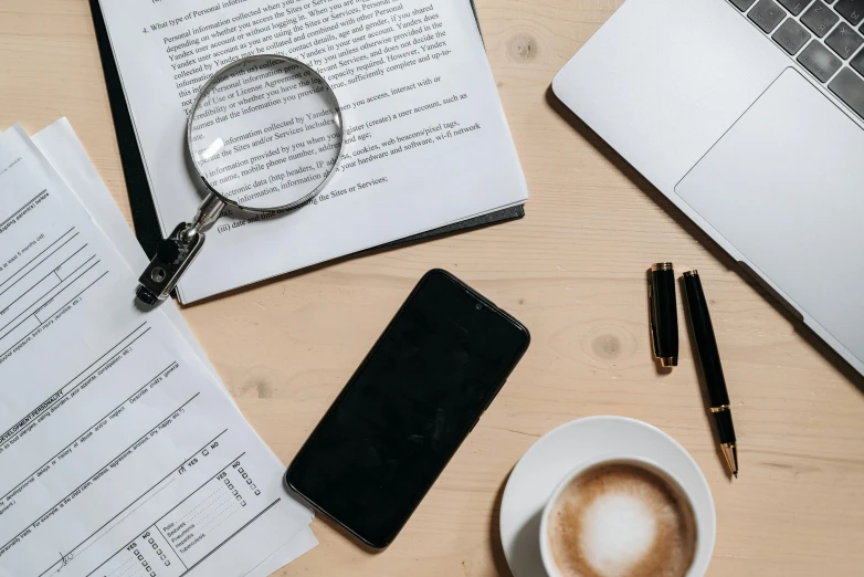 a laptop computer sitting on top of a wooden table next to a cup of coffee, trending on pexels, analytical art, magnifying glass, papers on table, 9 9 designs, phone photo