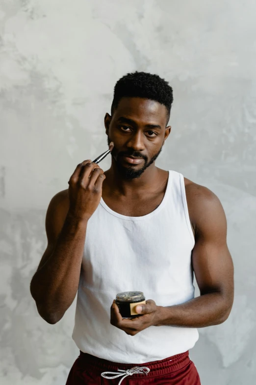 a man in a white tank top talking on a cell phone, a character portrait, by Jessie Alexandra Dick, pexels contest winner, holding a paintbrush in his hand, ebony skin, photoshoot for skincare brand, he is wearing a black t-shirt