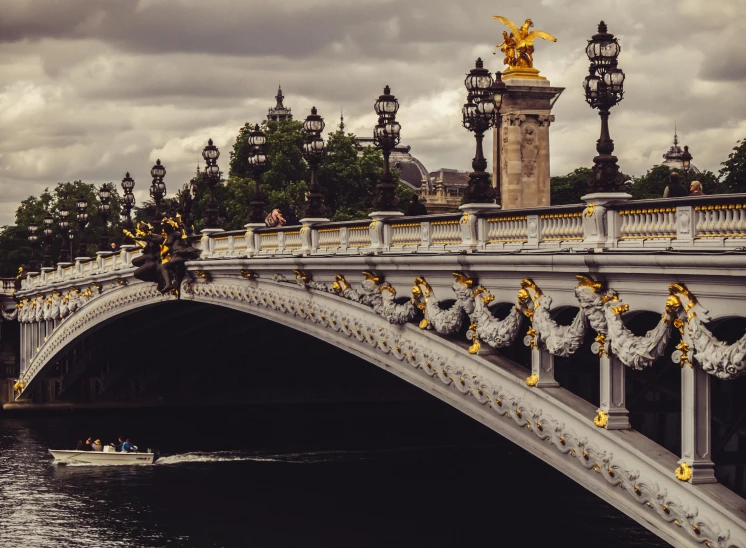 a bridge over a body of water under a cloudy sky, by Raphaël Collin, pexels contest winner, neoclassicism, paris hotel style, ornate with gold trimmings, a quaint, a cozy