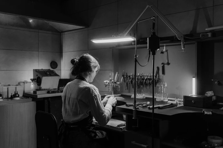 a black and white photo of a woman in a lab, by Kristian Zahrtmann, pexels contest winner, arbeitsrat für kunst, professional gunsmithing, rembrandt lighting scheme, jewelry lighting, evening light