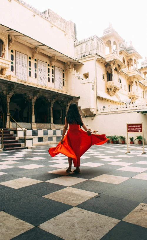 a woman in a red dress walking in a courtyard, pexels contest winner, of indian princess, stepping on the city, all around, square