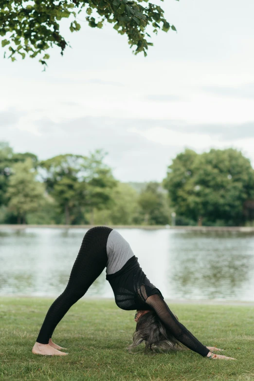 a woman doing a handstand in a park, by Rachel Reckitt, on a lake, doing splits and stretching, grey, black