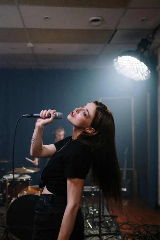 a woman singing into a microphone in a room, an album cover, inspired by Elsa Bleda, pexels contest winner, realism, sasha grey, performing a music video, rock star, schools