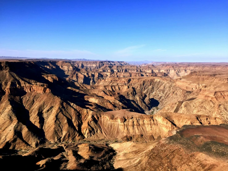 an aerial view of a canyon in the desert, blue sky, bixbite, towering high up over your view, slightly golden