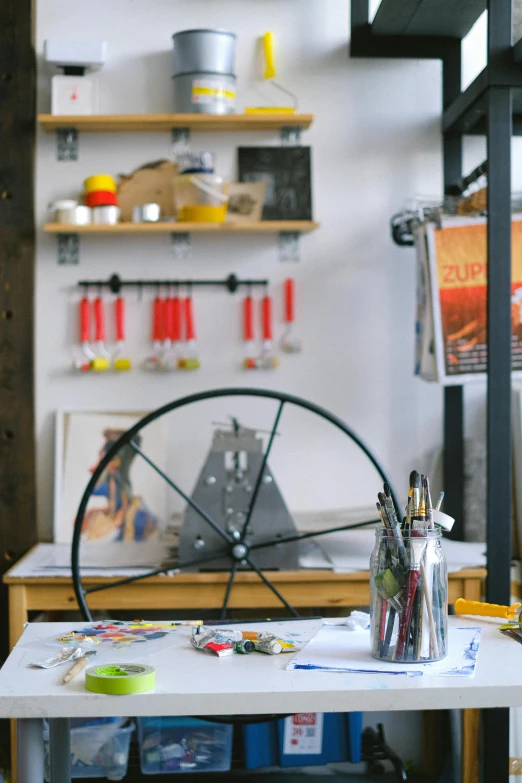 a bicycle wheel sitting on top of a white table, a silk screen, art materials, architect studio, hanging, tools