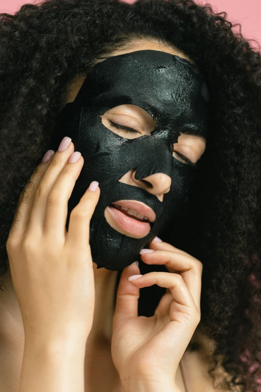 a woman with a black mask on her face, hands on face, face and body, with textured hair and skin, medium - shot