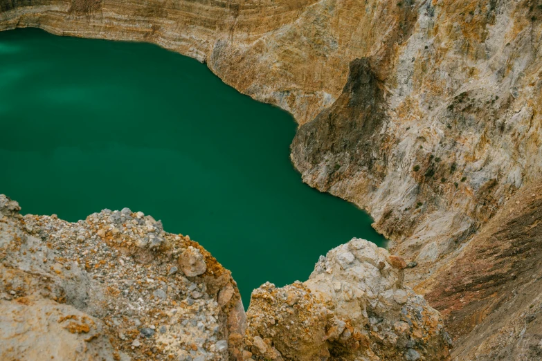 a man standing on top of a cliff next to a lake, a picture, trending on unsplash, australian tonalism, in dusty open pit mine, cyan and gold scheme, emeralds, crater