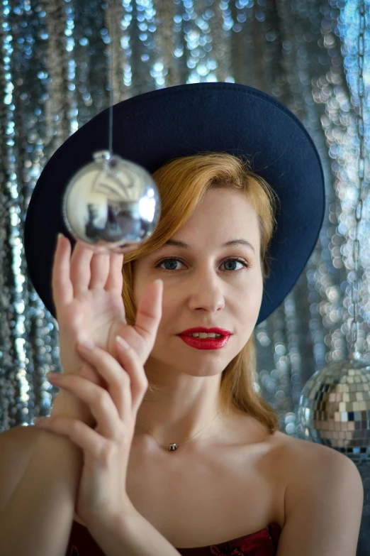 a woman holding a mirror ball in front of her face, by Julia Pishtar, reddit, wearing cylinder hat, christmas, blue and silver, pinup model