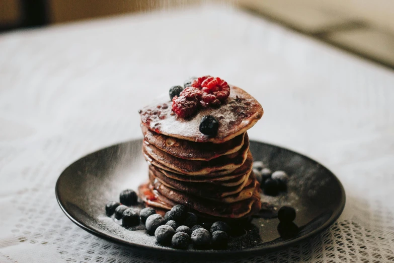 a stack of pancakes sitting on top of a black plate, unsplash, wild berries, chocolate, on a wooden table, background image