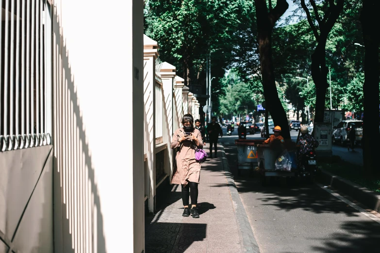 a woman walking down a sidewalk with a frisbee in her hand, pexels contest winner, visual art, light brown trenchcoat, south jakarta, looking at his phone, milan jozing